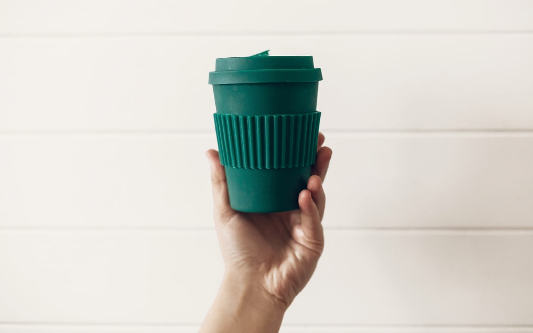 Zero waste concept. Hand holding stylish reusable eco coffee cup on white wooden background. Green Cup from natural  bamboo fiber. Ban single use plastic. Make a choice.
