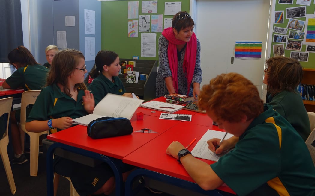 Principal leans over table with children writing in books.