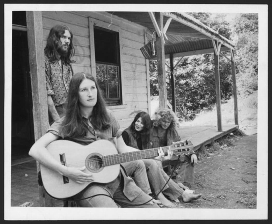 An image of the commune at Jerusalem. A young woman sits playing a guitar on the front porch.