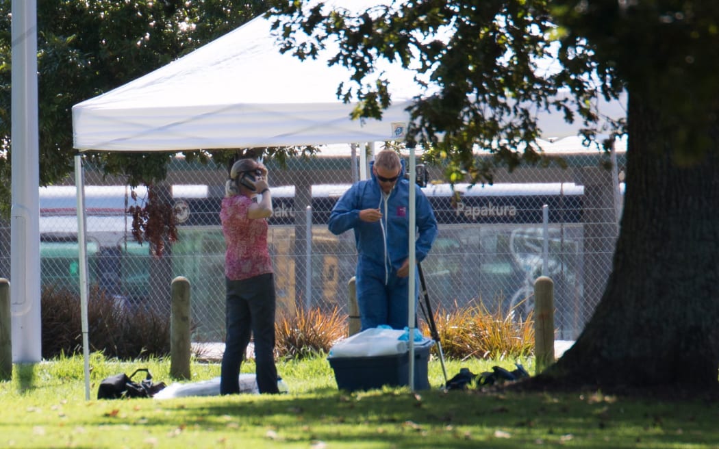 Police gather evidence opposite the train station in Papakura after a shooting left one man dead and another seriously injured.
