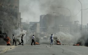 Protesters gesture towards police officers (not seen) as they burn tyres in Jeppestown, Johannesburg, on 11 July, 2021.