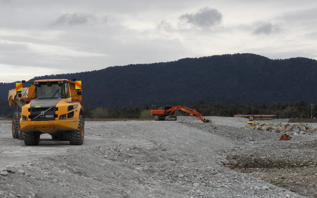 Work is continuing to widen, raise, and extend the Waiho River northern stopbank scheme which is expected to give about two decades relief for the town of Franz Josef nearby. The abandoned red roof of the Scenic Group Mueller Wing hotel can be seen in the distance, now below the natural riverbed height.