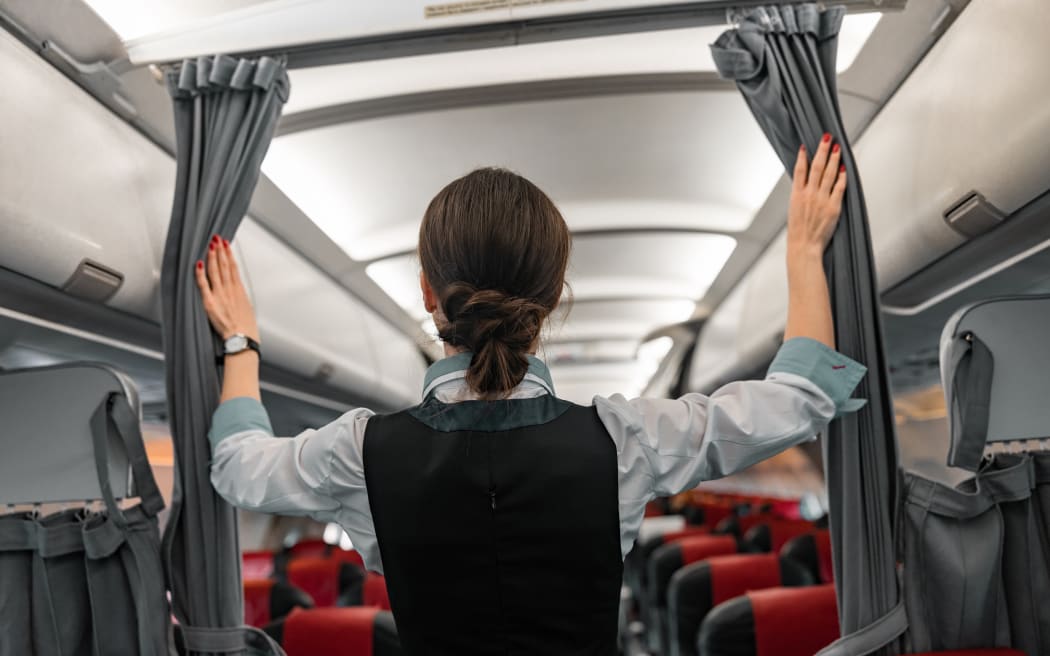 Female flight attendant welcoming passengers on board an airplane.