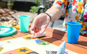 A person rolling the dice outdoors on a wooden table that has plates and cups.