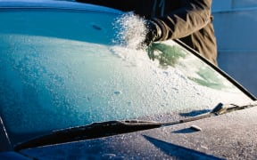 A man cleans frozen windshield by scratching, cold morning