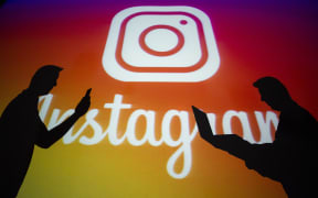 Silhouttes in front of the logo of 'Instagram'.