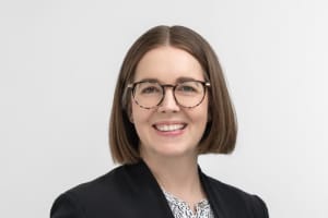 Rebecca Van Amber is a smiling woman with round tortoiseshell glasses and a brown bob with a middle parting.