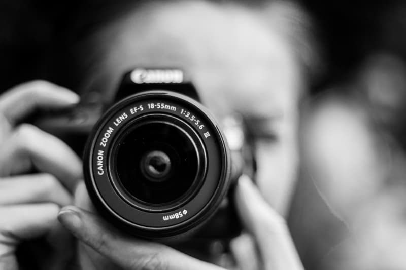 A person holding a camera to their fdace, in black and white.