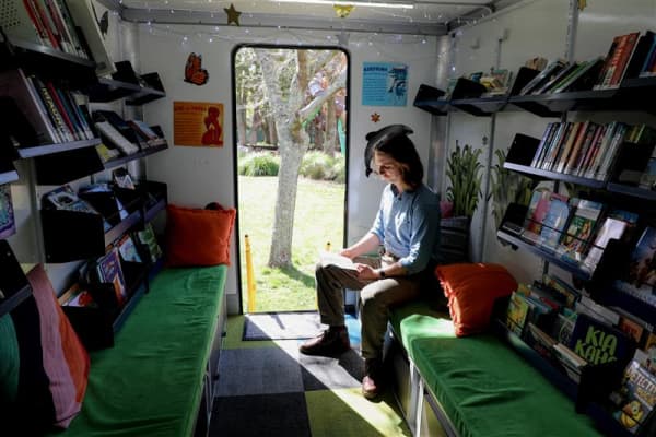Auckland librarian Gabriel Davey sitting in the mobile library and reading a book.