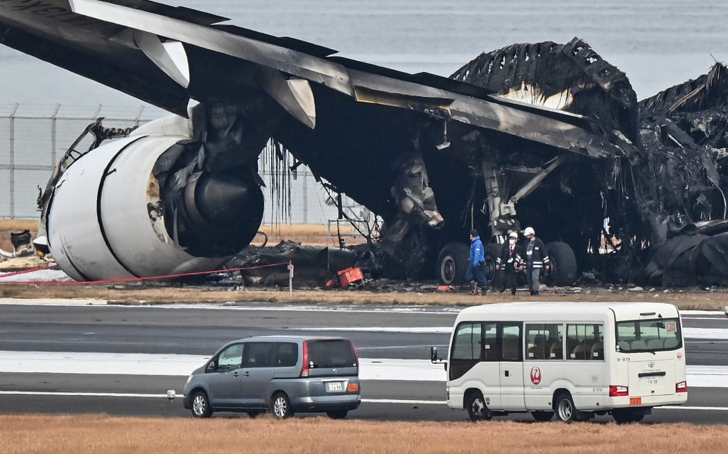 Officials look at the burnt wreckage of a Japan Airlines (JAL) passenger plane on the tarmac at Tokyo International Airport at Haneda in Tokyo on 3 January, 2024, the morning after it hit a smaller coast guard plane on the ground. Five people aboard the coast guard aircraft died in the fiery collision between the two aircraft.