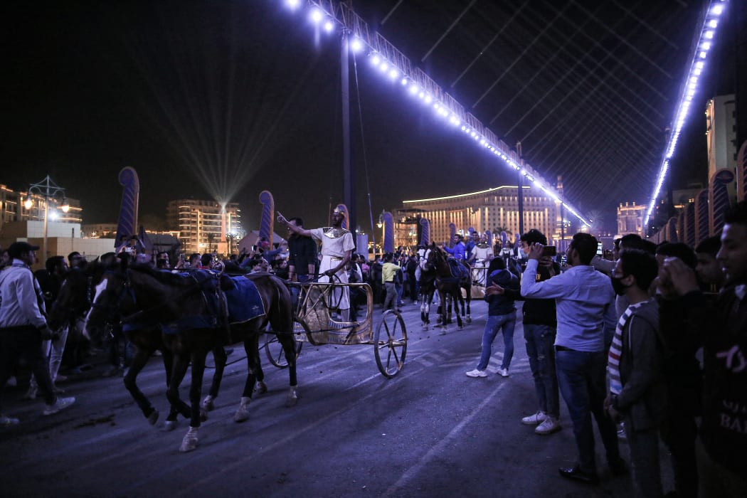 Crowds watching charioteer performers ride through Cairo, following the royal mummies.