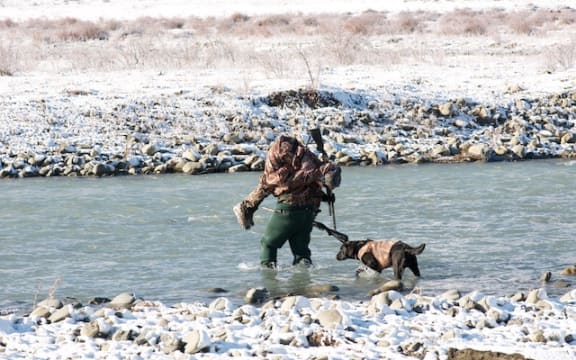 A father carries his son over a river as part of the Molesworth Goose Hunt.