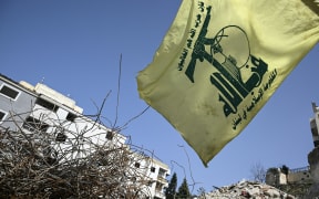 A flag of the Lebanese Shiite movement Hezbollah flutters above the rubble of a building that was hit in January by an Israeli strike in the southern Lebanese village of Qannarit, on February 16, 2026. Despite a November 2024 truce that sought to end more than a year of hostilities between Israel and Hezbollah, Israel has kept up regular strikes on Lebanon, usually saying it is targeting the Iran-backed group. (Photo by Joseph EID / AFP)