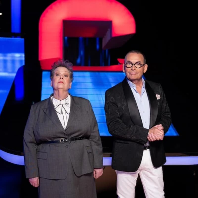 Anne Hegerty and Paul Henry stand confidently in front of a neon TV set.