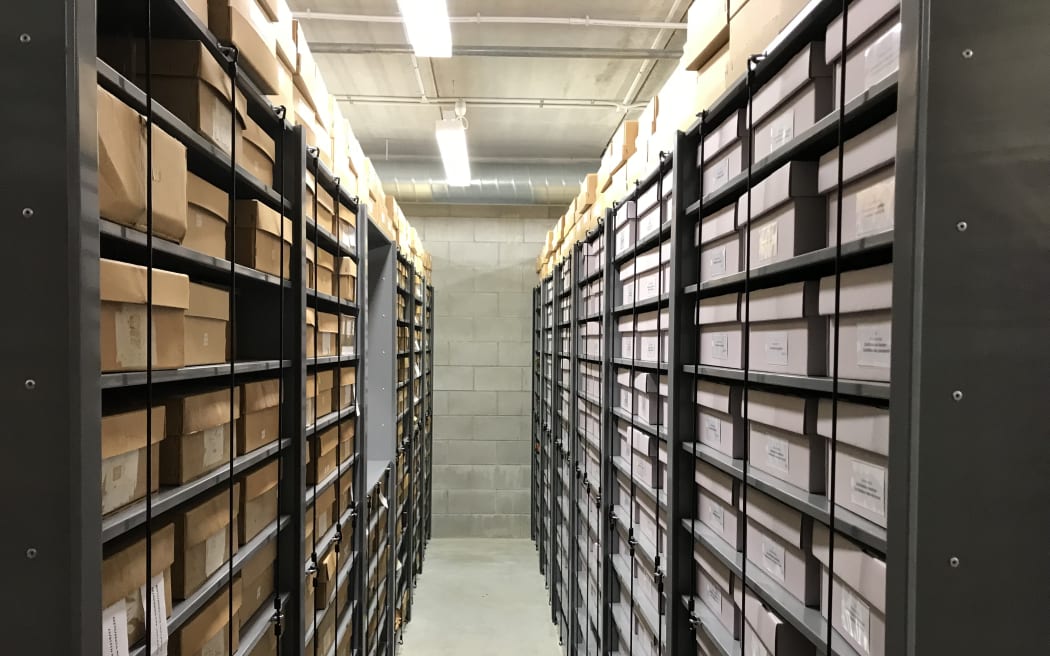 Looking down an an aisle with metal stacks on either side. All spaces are filled with cardboard boxes with labels on the front.