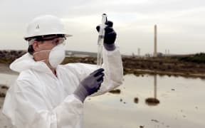Worker in a protective suit examining pollution in the water at the industry.