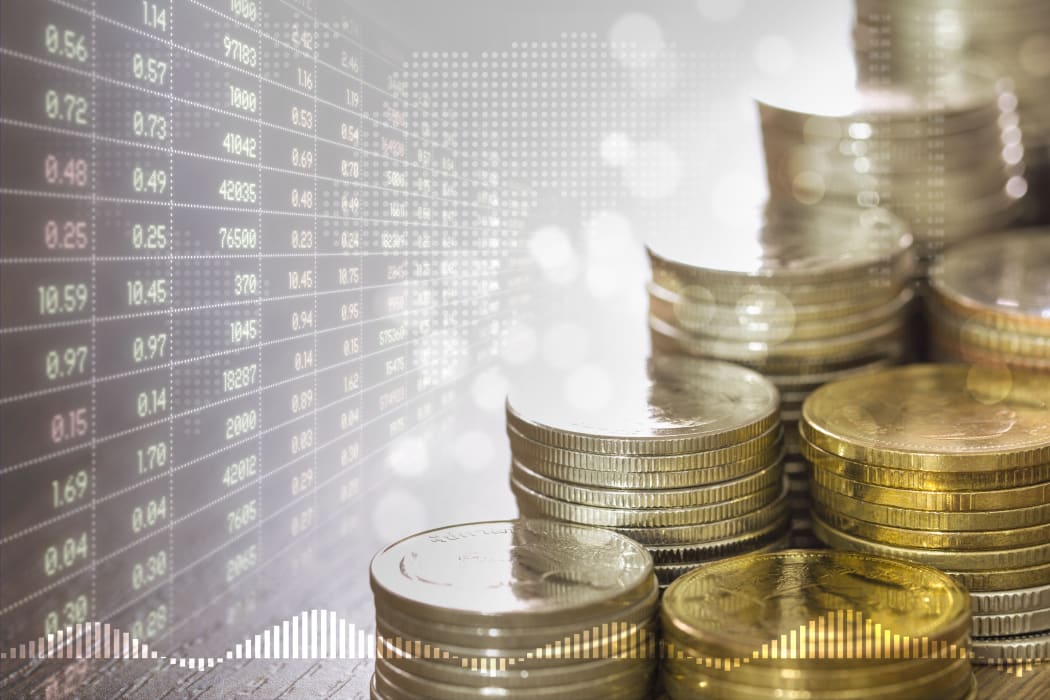 Stacks of coins money and faded stock trading board in golden light and soft bokeh with digital world map on background