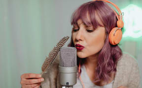A woman with pink hair blows into a microphone.