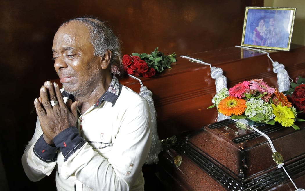 Baby Joseph Gomes prays standing next to coffins of his family members killed in the Easter Sunday bombings in Colombo, Sri Lanka, Tuesday, April 23, 2019.