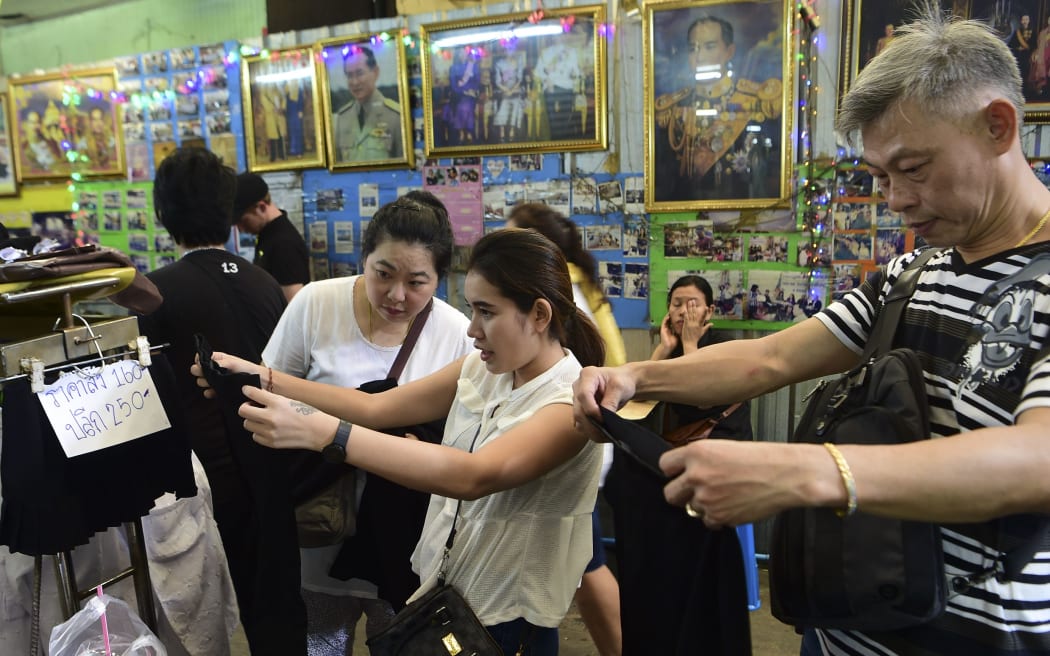 Mourners browse black dresses in a shop next to photos of the late Thai King Bhumibol Adulyadej in Bangkok on October 15, 2016.