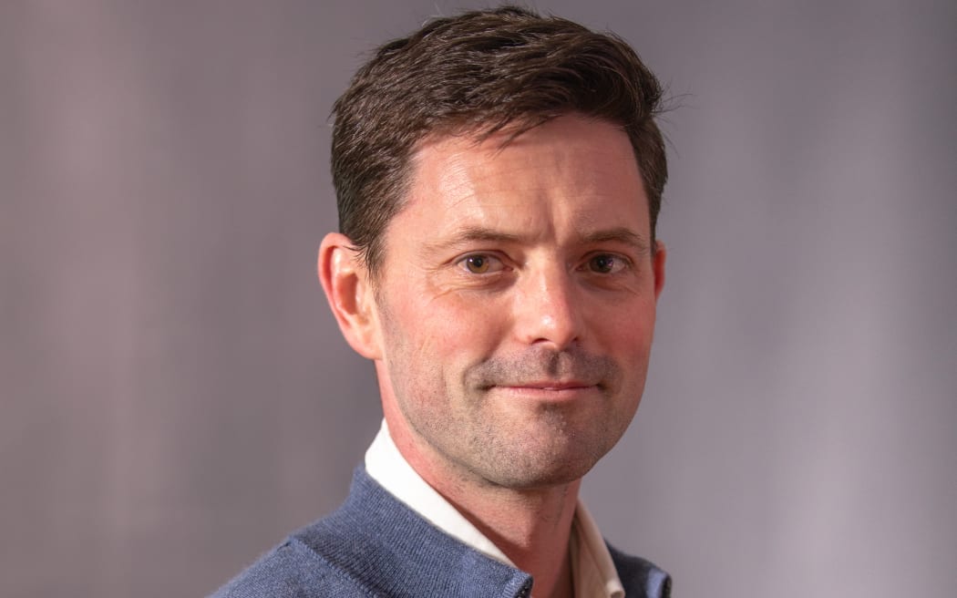 Image of Mike Wesley-Smith smiling at the camera in front of a grey background.
