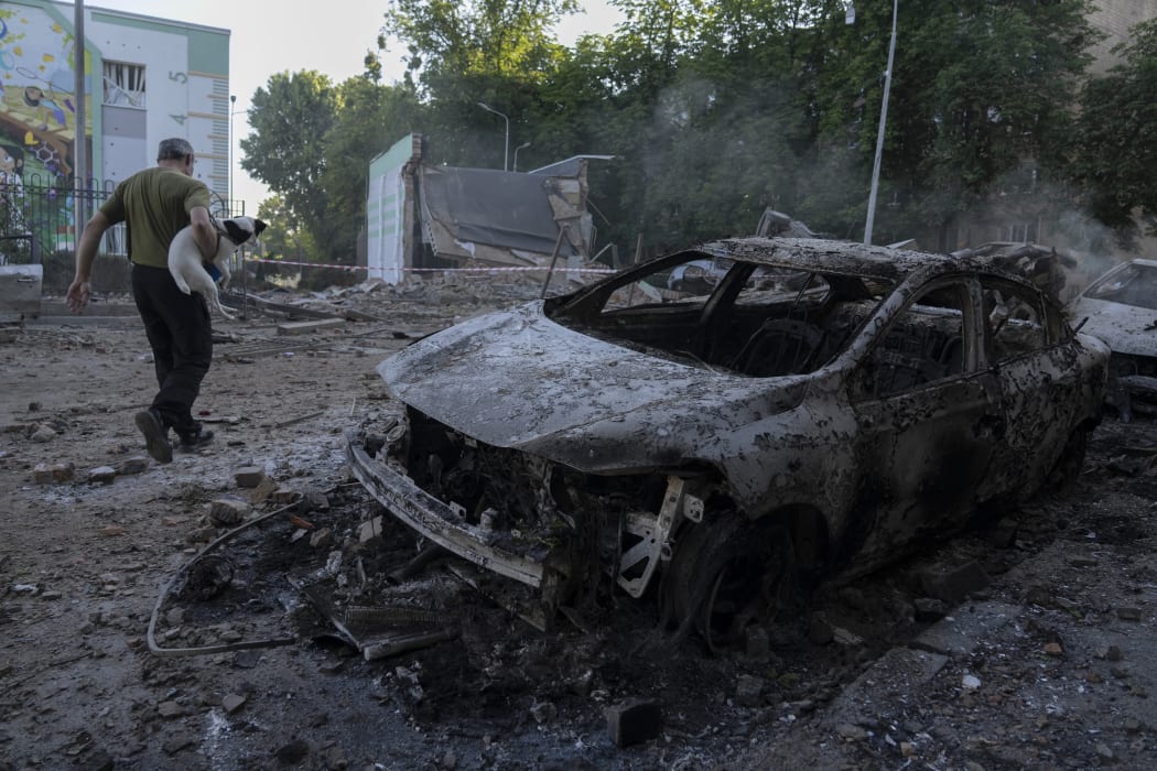 A man carrying a dog walks past the wreckage of cars following mass Russian drones and missile strike on the Ukraine's capital Kyiv on July 4, 2025, amid the Russian invasion of Ukraine. Kyiv said on July 4 that Russia had launched its largest overnight aerial attack on Ukraine over the more than three-year invasion. A representative of Ukraine's air force Yuriy Ignat said the barrage of 550 drones and missiles was a record, adding "this is the largest number that the enemy has used in a single attack." (Photo by OLEKSII FILIPPOV / AFP)