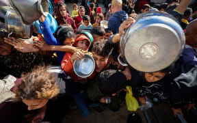 Displaced Palestinians gather to receive food portions at a charity kitchen in the Nuseirat refugee camp in the central Gaza Strip on December 20, 2025.