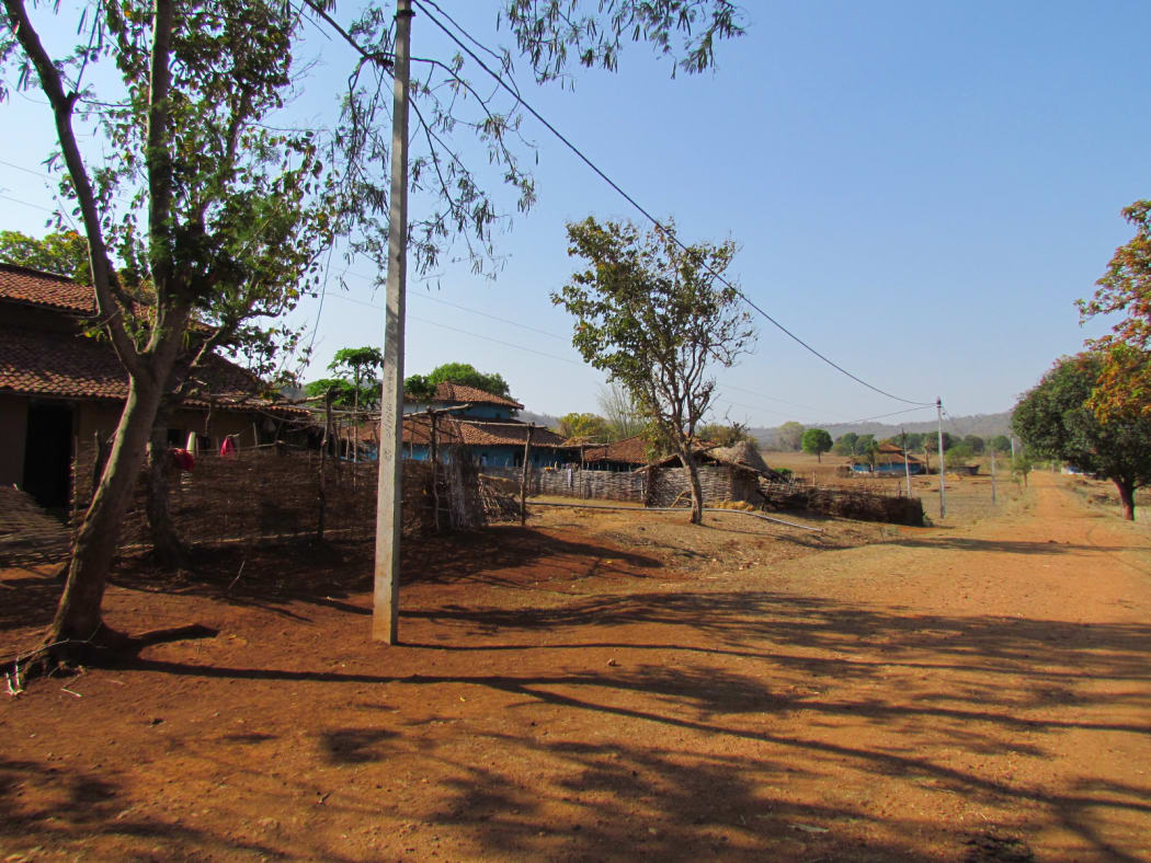 Wide dirt road with  local material huts alongside under bright blue sky