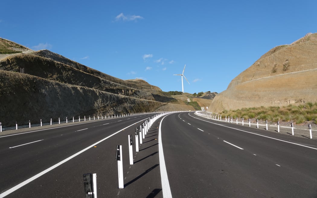 The four-lane highway snakes through hills and between wind turbines.