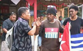 Ben Didiomea displays the West Papuan flag as Indonesian staff try  to usher him away.
