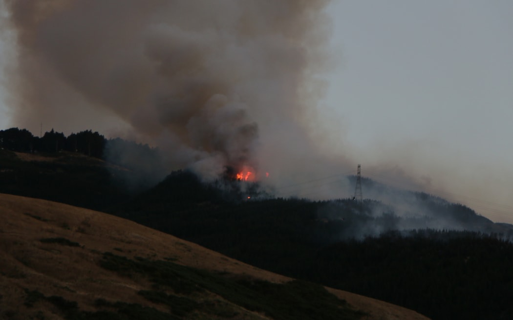 As night falls, flames from the Port Hills fire on 14/2/2024 become more apparent.