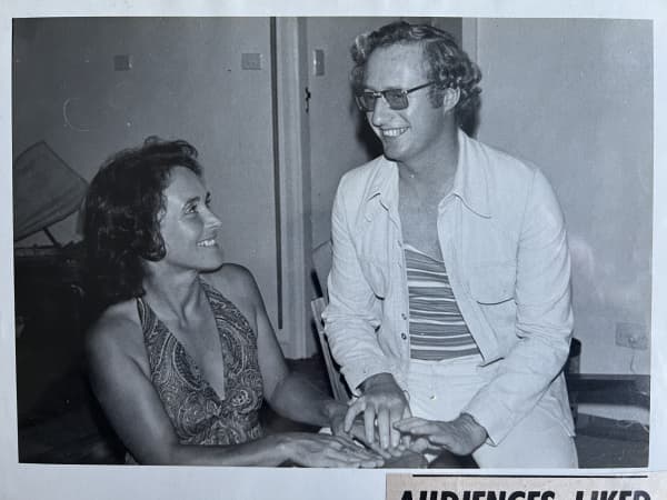A young man and woman smile at each other in a black and white photo.