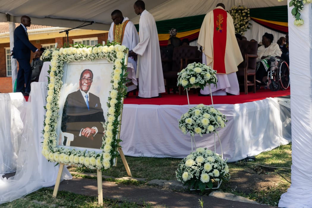 Priests stand near a portrait of Robert Mugabe during the burial of the former Zimbabwe leader at his home village in Kutama, on September 28, 2019.