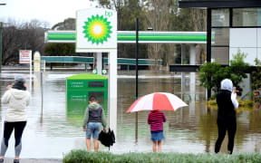 People stand next to a flooded petrol station due to torrential rain in the Camden suburb of Sydney on July 3, 2022. - Thousands of Australians were ordered to evacuate their homes in Sydney on July 3 as torrential rain battered the country's largest city and floodwaters inundated its outskirts. (Photo by Muhammad FAROOQ / AFP)