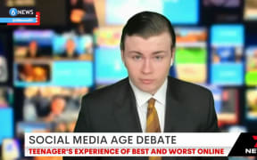 Leo is seated for a live interview with a green screen of a busy newsroom behind him. He wears a suit and has AirPods in to hear the presenter.