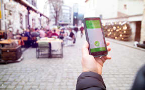 Vaccinated person using a digital vaccination or immunisation certificate on a smartphone at a restaurant terrace.