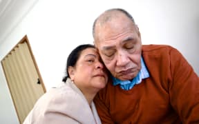 An older woman with a man wearing a red cardigan.