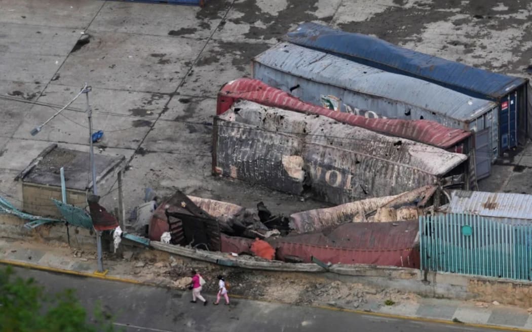 Pedestrians walk past destroyed containers lay at La Guaira port after explosions were heard in Venezuela, Saturday, Jan. 3, 2026.