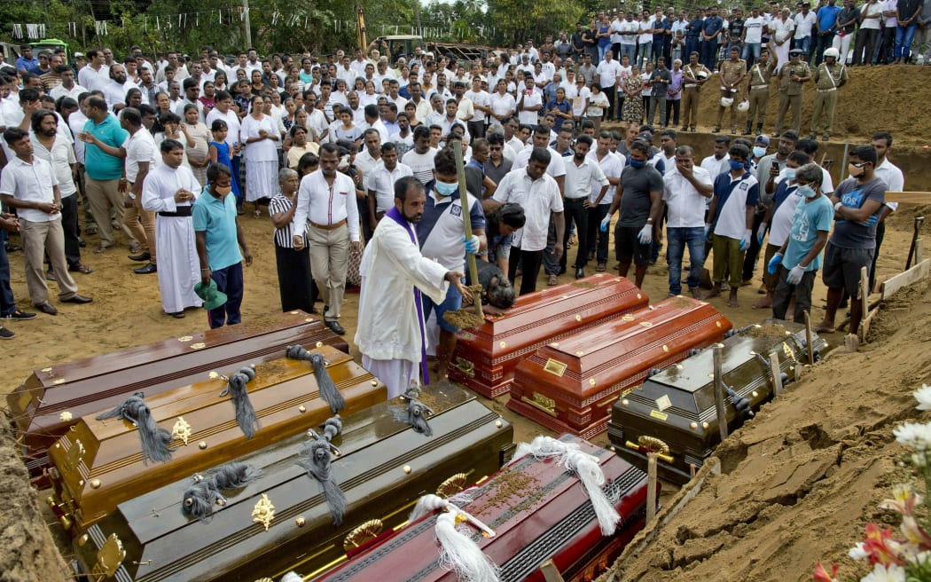 A priest conducts religious rituals during a mass burial for Easter Sunday bomb blast victims in Negombo, Sri Lanka, Wednesday, April 24, 2019.