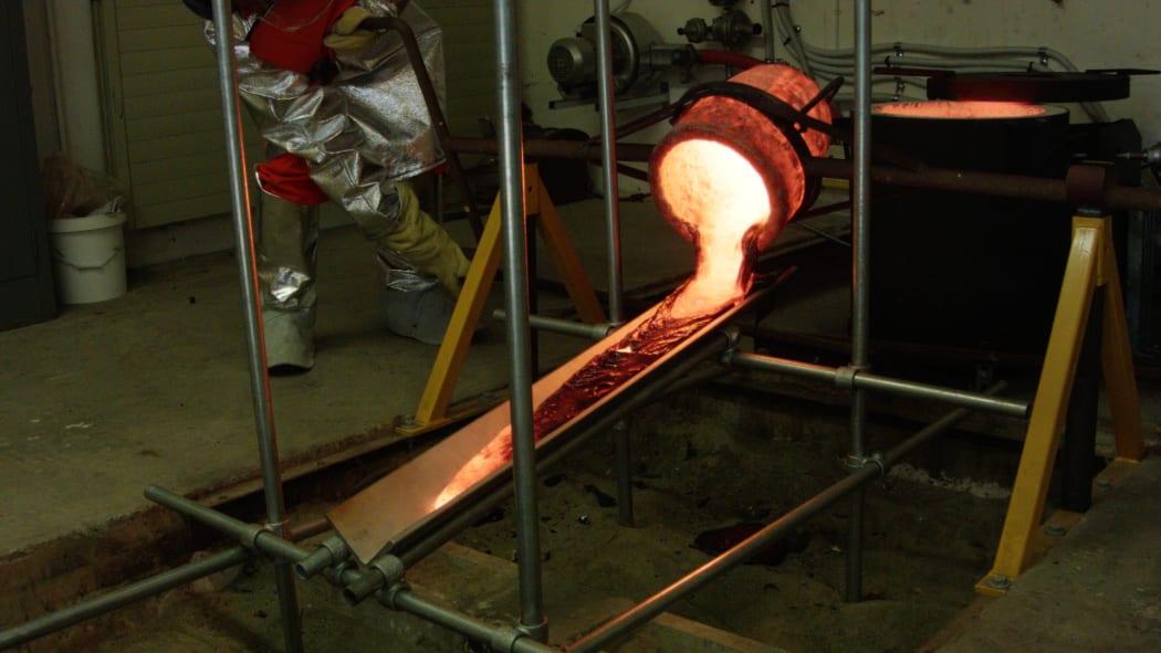 Molten lava pouring out the crucible down the tilted metal plate and beginning to cool down.