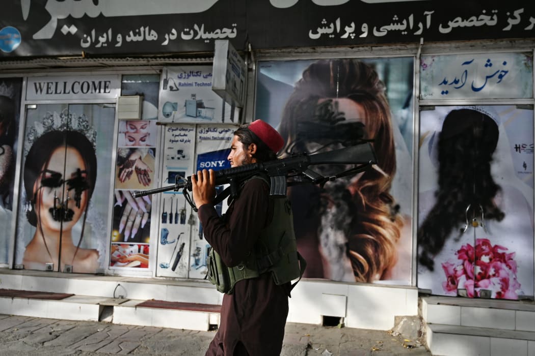 A Taliban fighter walks past a beauty salon with images of women defaced using spray paint in Shar-e-Naw in Kabul on 18 August 2021.
