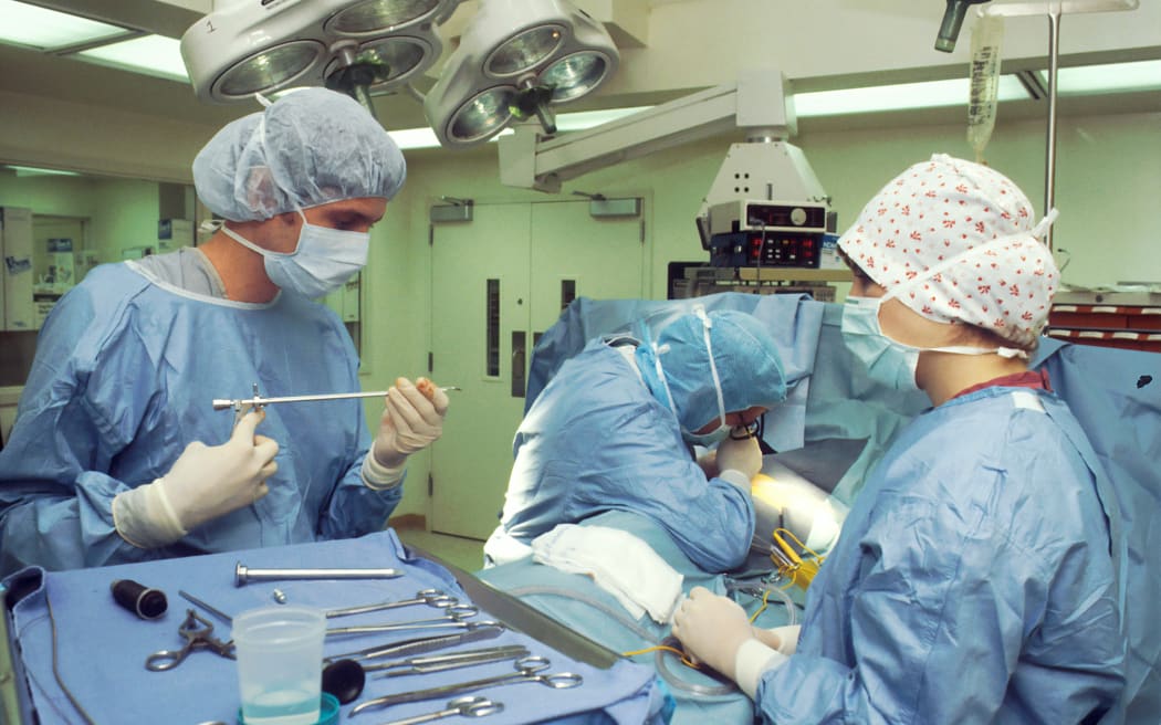 Two surgeons and a nurse perform a thoracoscopy in a hospital operating theatre.