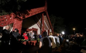 Te Whare Runanga is lit up as hundreds gather in the dark before it on the Waitangi Treaty Grounds.