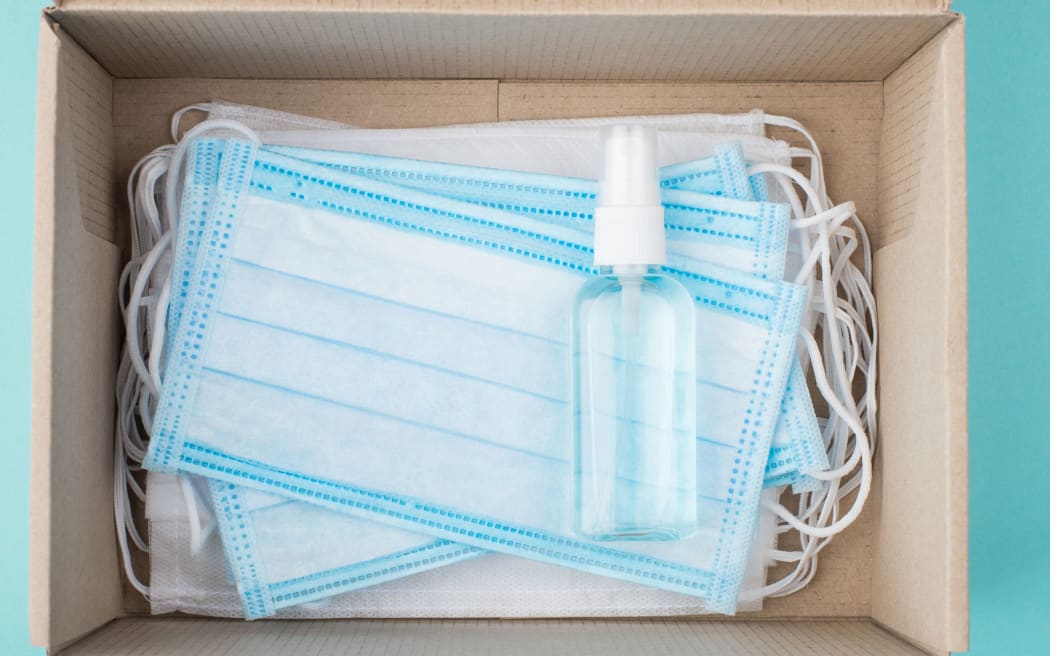 Firts ait kit concept. Top above overhead view photo of a box full of masks and a bottle of hand sanitizer isolated on turquoise background