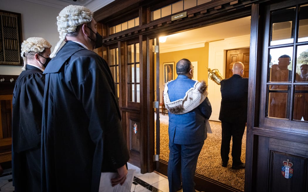 The newly elected Speaker Adrian Rurawhe (heralded by the Serjeant at arms and accompanied by his Clerks) waits at the door of Government House to be summoned by the Governor General for confirmation.
