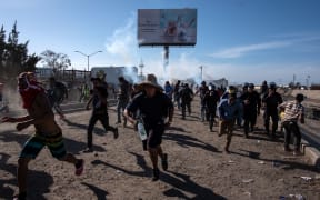 Central American migrants - mostly Hondurans - run along the Tijuana River near the El Chaparral border crossing in Tijuan, after the US border patrol threw tear gas from the distance to disperse them.