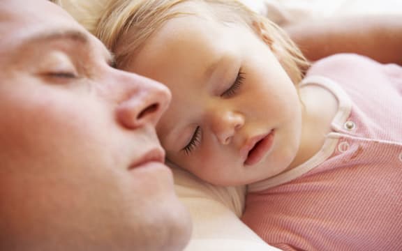 A photo of a father and daughter sleeping in bed