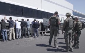 This image from video provided by US Immigration and Customs Enforcement shows manufacturing plant employees waiting to have their legs shackled at the Hyundai Motor Group’s electric vehicle plant, in Ellabell, Georgia, on September 4.