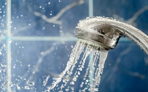 Showerhead with flow of water spilling out on blue background