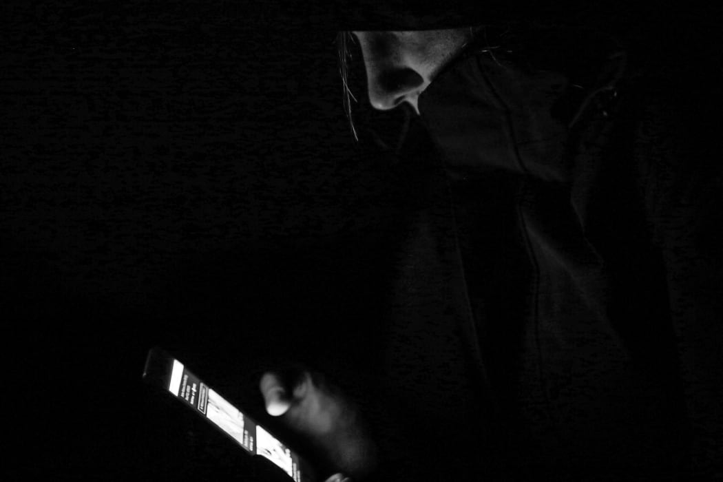 Hoody wearing young person peruses phone in the dark